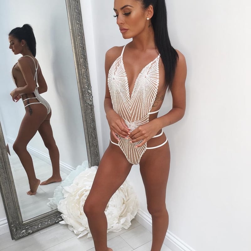 Woman wearing a white crochet swimsuit standing in front of a mirror.